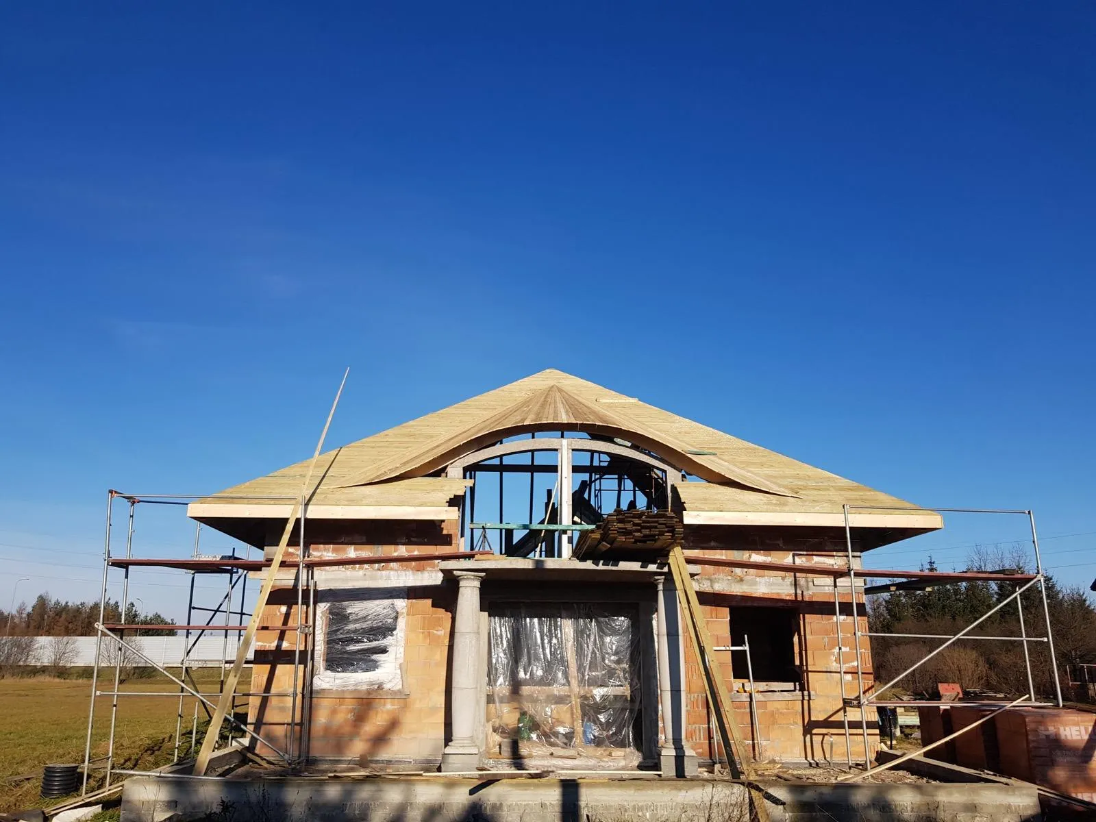 Front budynku z charakterystyczną łukową linią więźby i wyraźnie zarysowaną geometrią dachu.