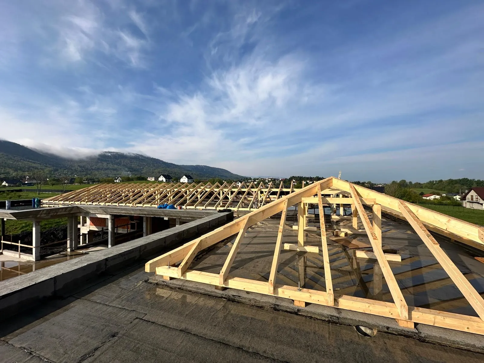 Etap montażu więźby przed wykonaniem poszycia, z dobrze widocznym rytmem krokwi i podpór.