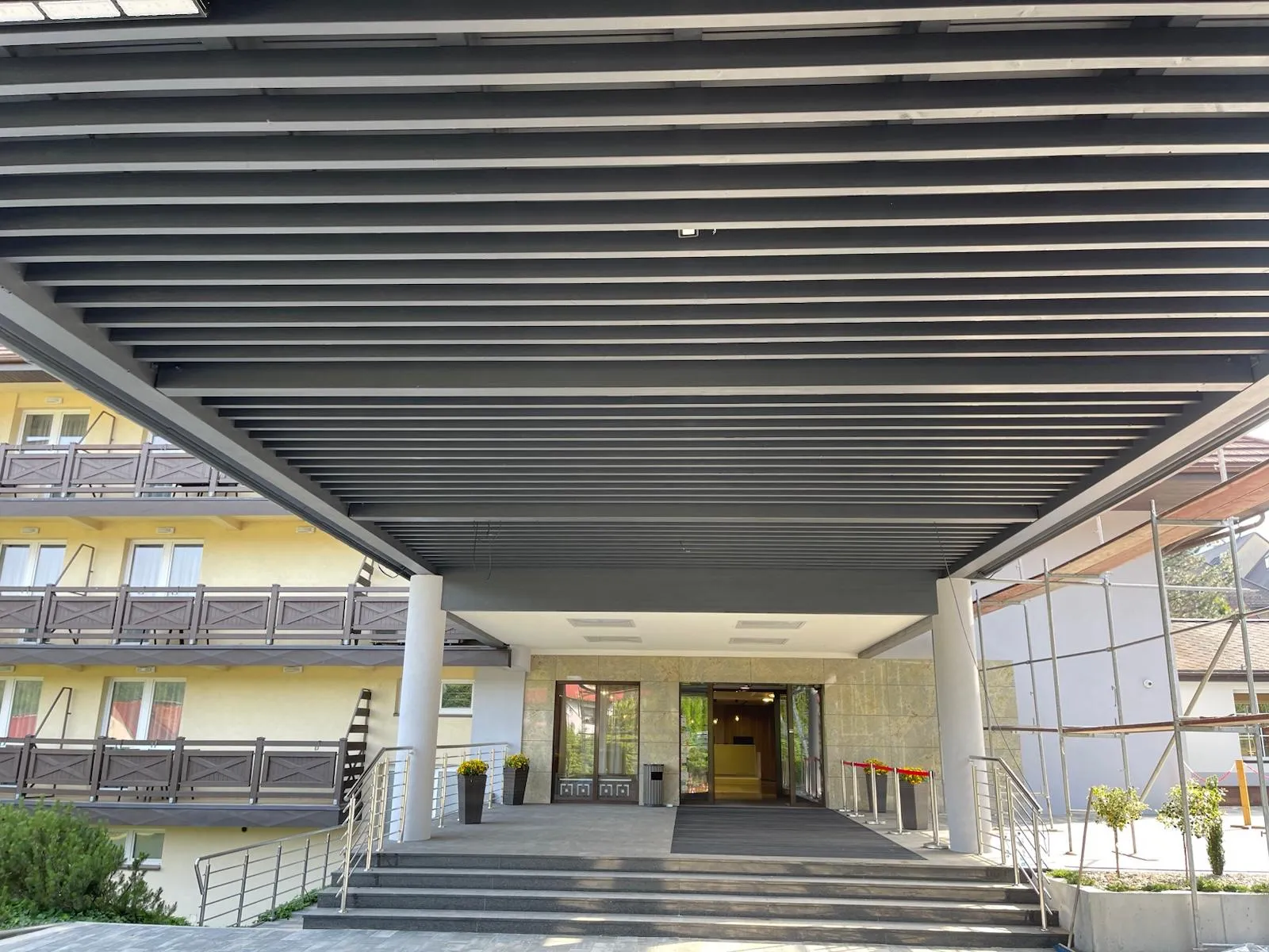 Szeroki widok spod zadaszenia z czytelnym układem belek, słupów i proporcji całej konstrukcji.